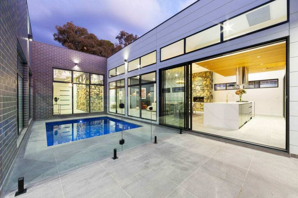 Homes by Howe, knock down rebuild, Deakin, open plan living area looking out onto courtyard pool, drystone wall fireplace