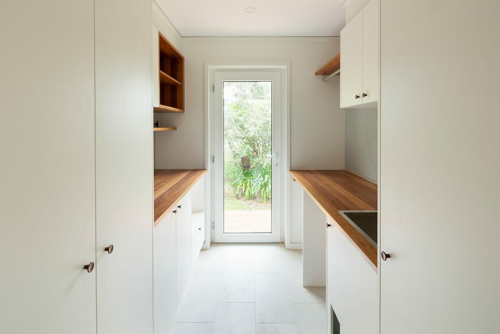 Homes by Howe, renovation, Cook, laundry, white tiling, floor to ceiling white cabinetry, wooden benchtops and large sink looking out of glass back door