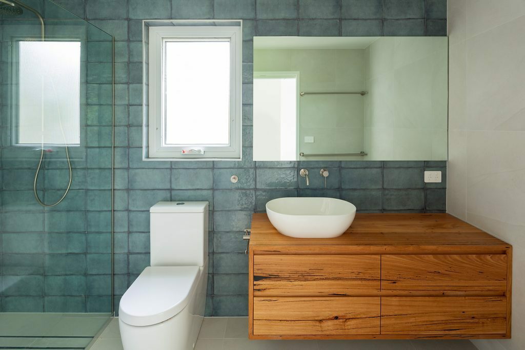 Homes by Howe, renovation, Cook, bathroom, teal tiles, wooden vanity, mirror and window above toilet