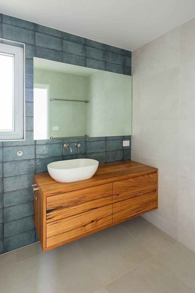 Homes by Howe, renovation, Cook, bathroom with teal coloured wall tiles and wooden vanity with white basin and mirrors on the wall